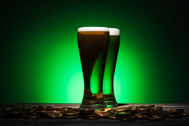 glasses of green beer standing near golden coins on green background - Foto, immagini