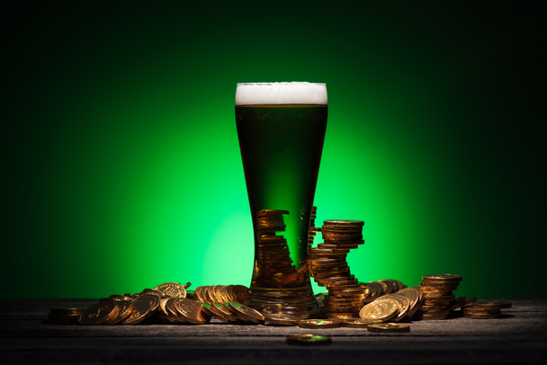 vetro di birra irlandese in piedi su tavolo di legno vicino monete d'oro su sfondo verde
 - Foto, immagini