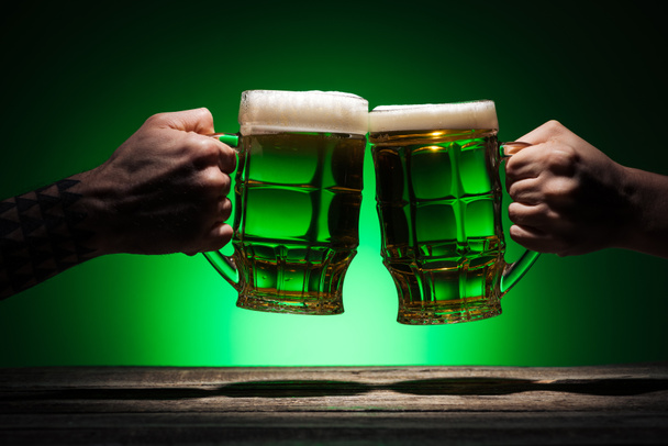 cropped view of male friends clinking with glasses of irish ale on st patricks day on green background - Photo, image