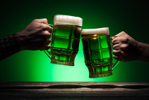 cropped view of friends clinking with glasses of irish ale on green background - Foto, Bild
