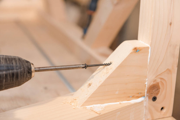 A man is screwing a screw into a wooden table. Carpentry workshop. Work with a screwdriver. Work tool. - Φωτογραφία, εικόνα