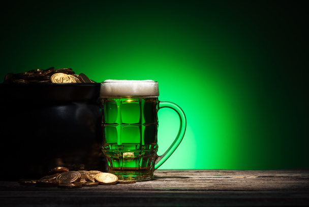 glass of ale near pot with golden coins on st patricks day on green background - Foto, afbeelding