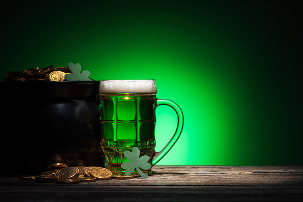 glass of ale near pot with gold and shamrocks on st patricks day on green background - Φωτογραφία, εικόνα