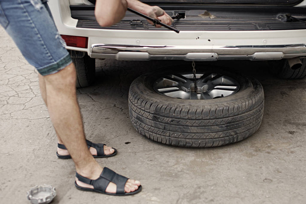 Výměna kola na auto, auto mechanik v džínách šortky a sandály vyndání Nástroj pro montáž - Fotografie, Obrázek