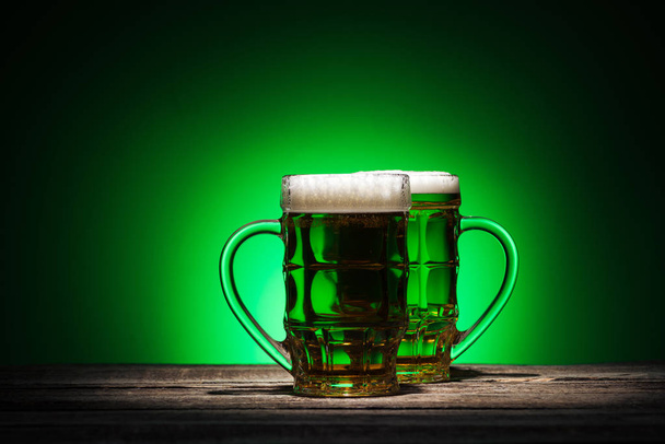 bicchieri di lager verde in piedi su tavolo di legno su sfondo verde
 - Foto, immagini