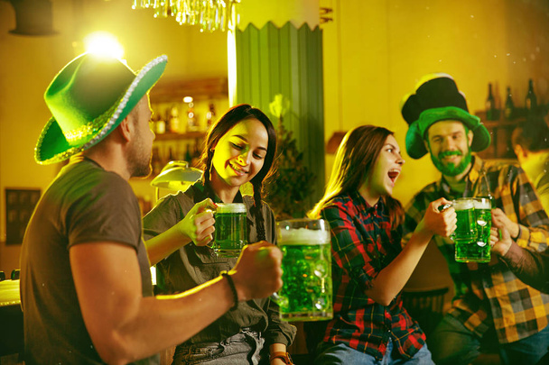 Saint Patricks Day Party. Happy friends is celebrating and drinking green beer. Young men and women wearing a green hats. Pub Interior. - Foto, immagini