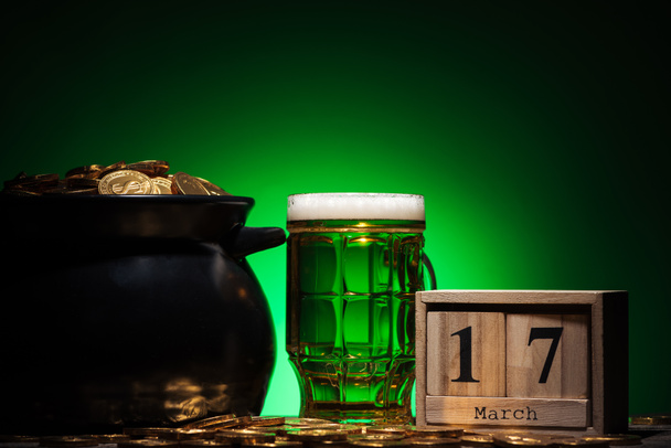 Irské pivo poblíž zlatých mincí v hrnci a krychle kalendáři na zeleném pozadí - Fotografie, Obrázek