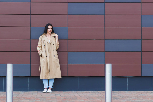 Женщина в бежевом пальто и джинсах на улице, мягкий фокус на фоне
 - Фото, изображение