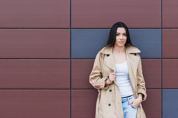 Beautiful woman in the beige coat and jeans on the street, soft focus background - Фото, изображение