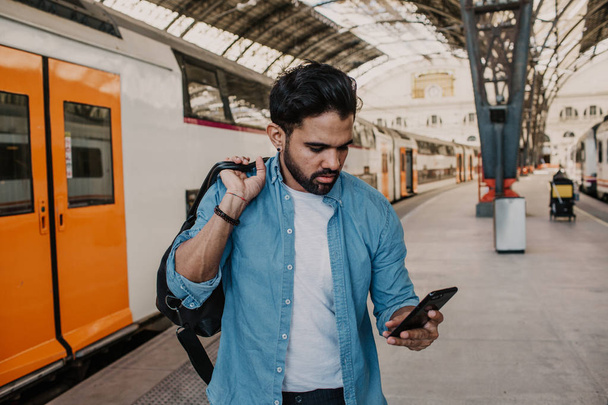 Attractive businessman sending message on his mobile phone.Casual professional entrepreneur using smartphone at hall of train station. - Valokuva, kuva