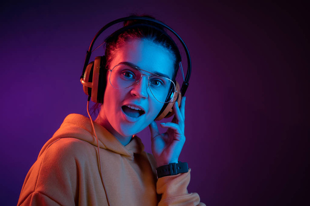 Fashion pretty woman with headphones listening to music over red neon background at studio. - Foto, immagini