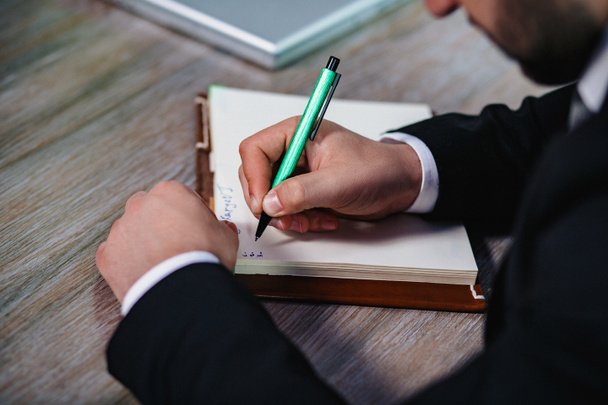 Mans hand in suit writing on notebook - Φωτογραφία, εικόνα