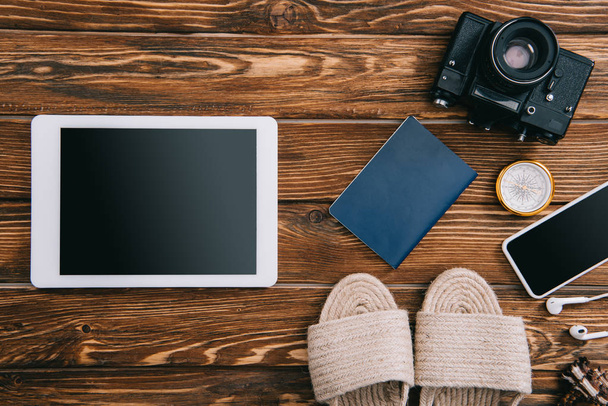 vista superior de dispositivos digitales, cámara de película retro, pasaporte y sandalias de mimbre en la superficie de madera
 - Foto, imagen