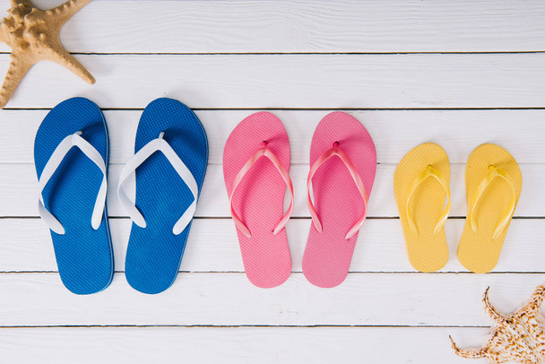 top view of yellow, blue and pink flip flops on white wooden background  - Foto, immagini