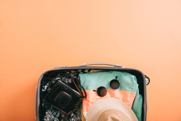 top view of suitcase with summer accessories and film camera on orange background - Fotó, kép