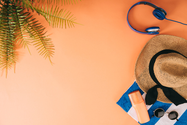 top view of summer accessories, headphones and sunscreen on orange background with palm leaves - Φωτογραφία, εικόνα