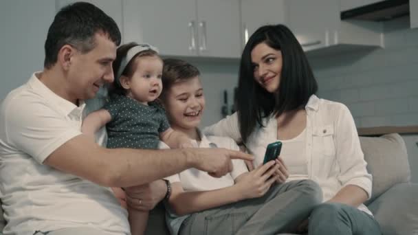 ευτυχισμένη οικογένεια χρησιμοποιώντας smartphone στον καναπέ στο σπίτι - Πλάνα, βίντεο