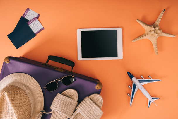 top view of summer accessories on travel bag, plane model, digital tablet and passports with tickets on orange background - Φωτογραφία, εικόνα