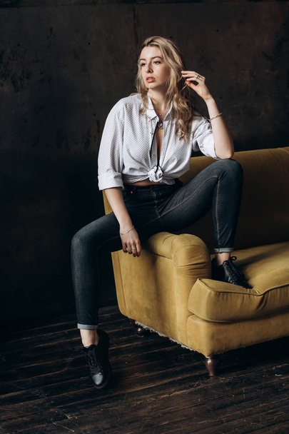 Portrait of a beautiful fashionable woman, blonde, jeans, on a yellow sofa - Fotografie, Obrázek