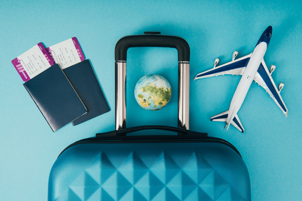 top view of globe and plane models, travel bag and passports with tickets on blue background - Photo, Image