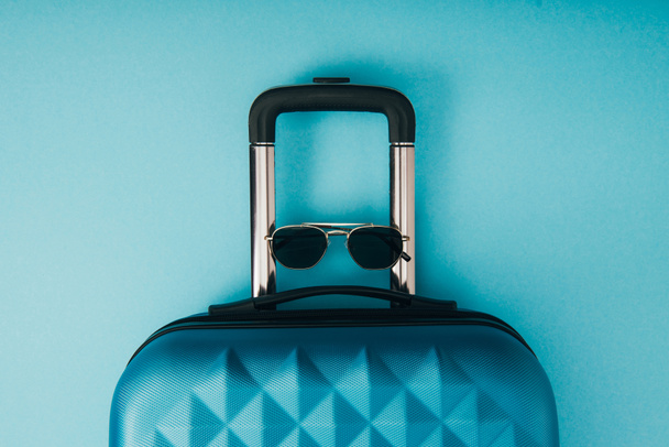 vista superior de gafas de sol y bolsa de viaje sobre fondo azul
 - Foto, Imagen