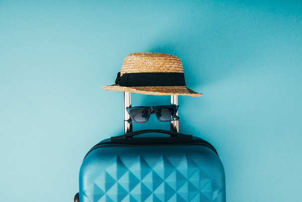top view of straw hat, sunglasses and travel bag on blue background - Photo, Image