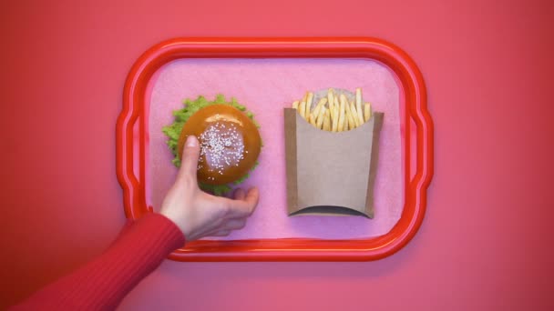 Female hands taking hamburger and french fries from tray on bright background - Filmati, video