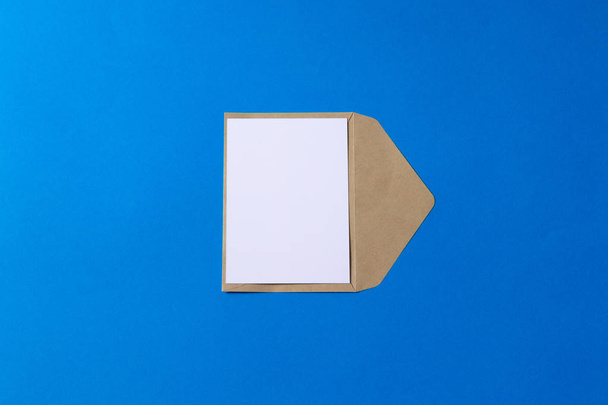 Lege witte kaart met bruin kraft papieren envelop sjabloon mock up op blauwe achtergrond - Foto, afbeelding