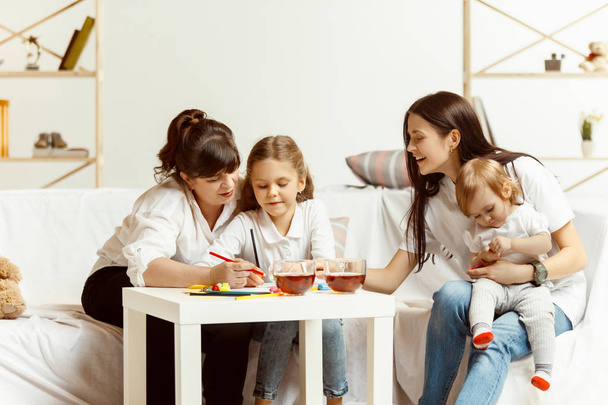Little girls, attractive young mother and charming grandmother are sitting at home - Fotoğraf, Görsel