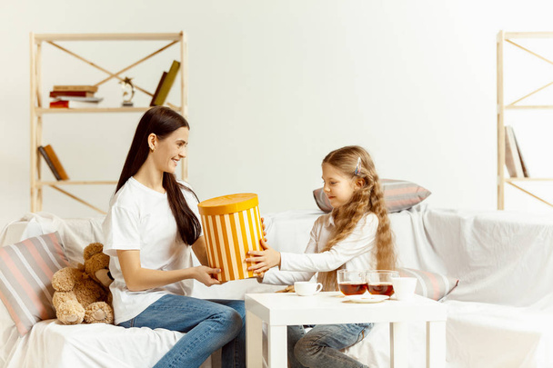 Little girl, attractive young mother are sitting at home - Фото, изображение