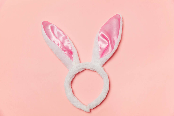 Gelukkig Pasen concept. Voorbereiding voor vakantie. Decoratieve bunny oren harige pluizig kostuum speelgoed geïsoleerd op trendy pastel roze achtergrond. Eenvoudige minimalisme plat leggen bovenaanzicht kopie ruimte - Foto, afbeelding