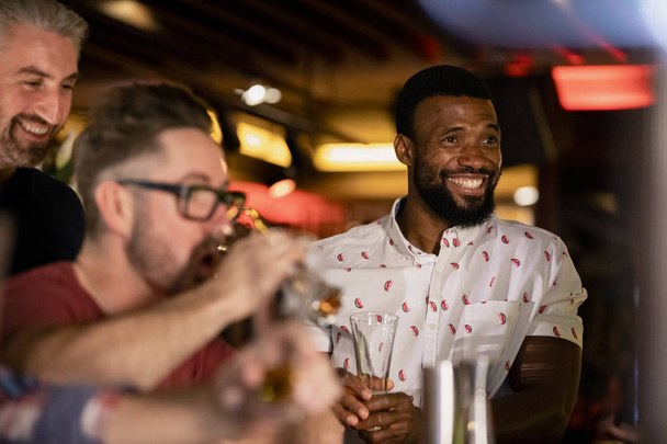 Three mid adult male friends enjoying a beer together in a bar.  - Foto, immagini