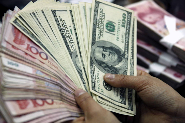 A Chionese bank clerk counts RMB yuan and US dollar banknotes at a bank in Huaibei, east Chinas Anhui province, April 13, 2010 - Photo, Image