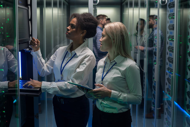 Két nő dolgozik egy adatközpontban, server szekrény sor - Fotó, kép