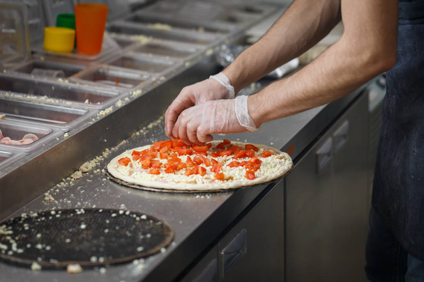 Бейкер кладет помидоры и сыр на корку пиццы в ресторане быстрого питания
 - Фото, изображение