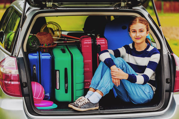 Zomervakantie, jong meisje in de kofferbak van de auto is klaar voor reizen voor familievakantie. - Foto, afbeelding