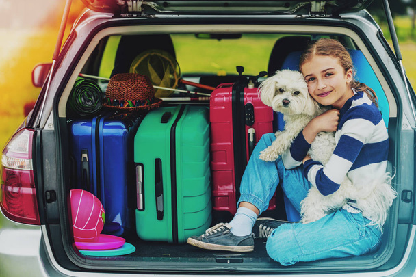 夏休み、車で犬と一緒に車のトランクで若い女の子が家族での休暇の旅行の準備. - 写真・画像