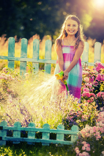 Fille ludique arrosant des fleurs avec de la pluie dans le jardin le jour d'été. Enfant utilisant un tuyau d'arrosage le jour ensoleillé au coucher du soleil lite. Petit jardinier jouant dans le jardin
. - Photo, image