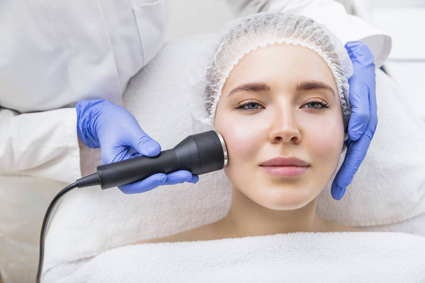 Beautician makes ultrasound massage procedure on female face - Фото, изображение