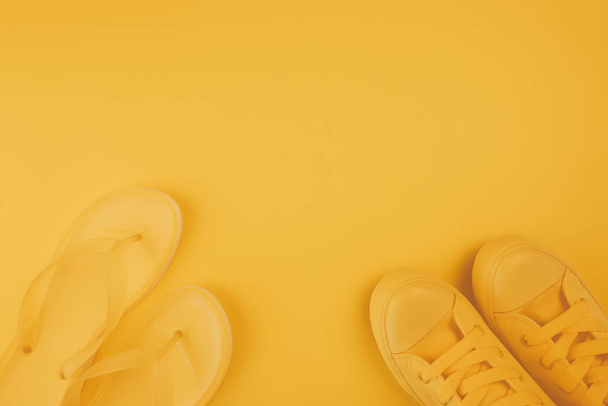 Summer footwear, yellow sneakers and flip flops on same color background with copy space - Foto, afbeelding