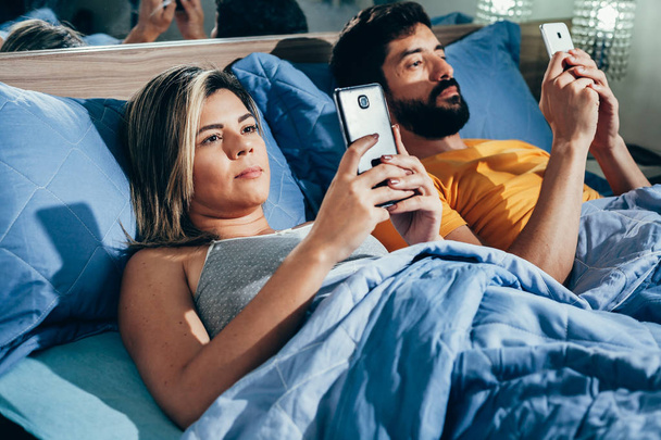 Молодая пара лежит в постели с помощью мобильного телефона
 - Фото, изображение