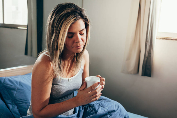 Sick woman sitting on her bed drinking tea or coffee - Foto, Imagem