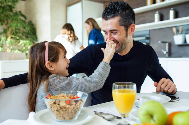 Shot of smiling cute father and daughter having fun while having breakfast in family in the kitchen at home. - Фото, зображення