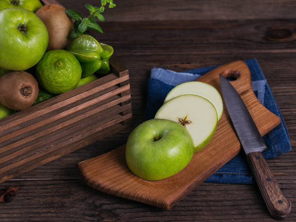 Concept of healthy food. Fresh green fruits in a box, green apple on cutting board. Dark wooden background. Set of green fruits for healthy diet and detox: apple, lime, kiwi, mango, carambola and mint - Foto, afbeelding