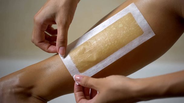 Female hand removing wax strip from leg, home depilation, beauty procedure - Fotó, kép