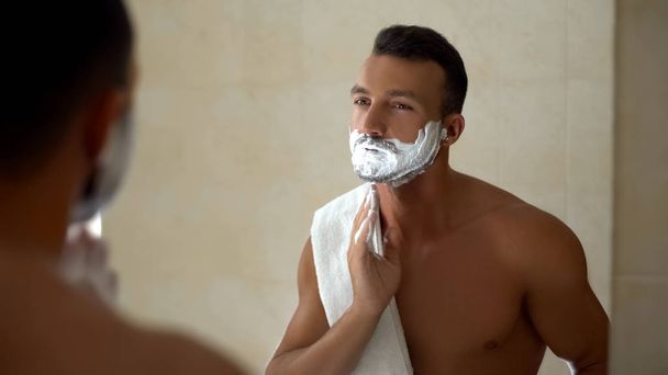 Homme appliquant de la crème à raser sur le visage et la barbe, prêt à changer d'apparence, de style
 - Photo, image