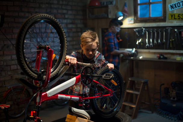 Tiro médio de dois meninos consertando uma bicicleta em uma garagem
 - Foto, Imagem