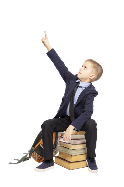 Schoolboy is sitting on books and showing thumb up, isolated on white background - 写真・画像