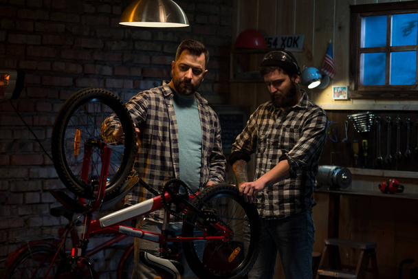 Kaksi miestä työskentelee polkupyörän korjaamossa.
 - Valokuva, kuva