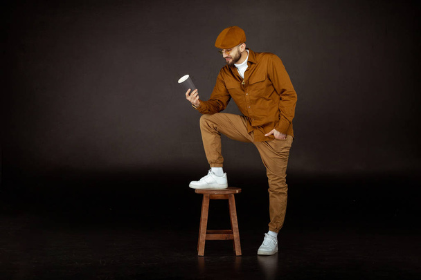 Serious man in beige hat standing on chair with one leg - Фото, зображення